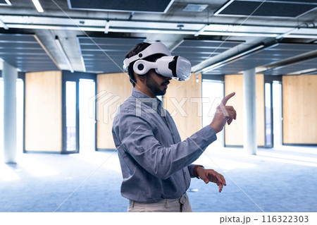 Using VR headset, man interacting with virtual interface in modern office, copy space 116322303