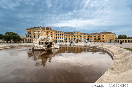 Vienna, Austria, August 20, 2022. Stunning shot of the Schonbrunn Palace, the characteristic yellow facade is reflected in the fountain located at the entrance of the residence. People. 116324365