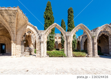Bellapais Abbey ruins showing gothic architecture with stone arches and cypress trees. Cyprus 116324416