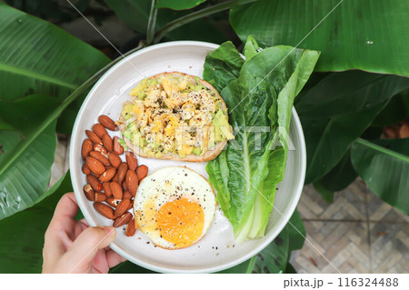 bread with egg and avocado topping with sunny side up egg , lettuce and almond 116324488