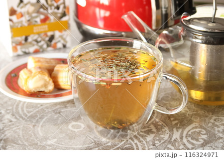 Herbal tea in glass cup. Teapot on table, vanilla eclair pie In kitchen. 116324971