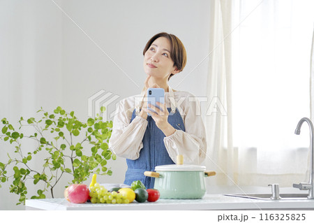 キッチンで想像しながらスマホを使う女性 116325825