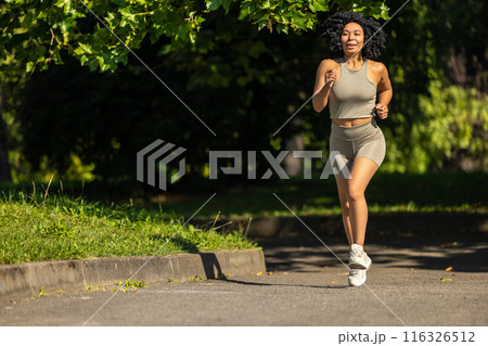 Woman in summer sportswear running in a sunny par and looking focused Woman in summer sportswear running in a sunny par and looking focused 116326512