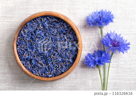 Dried blue cornflower petals in wooden bowl on linen fabric. Edible flowers of Centaurea cyanus, also known as bachelors button, flowers with intense blue pigment, used for tea and salad decorations. Dried blue cornflower petals in wooden bowl on linen fabric. Edible flowers of Centaurea cyanus, also known as bachelors button, flowers with intense blue pigment, used for tea and salad decorations. 116326616