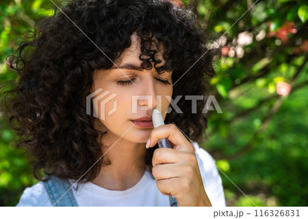 Dark-haired young woman using nasal spray while having allergy symptoms 116326831