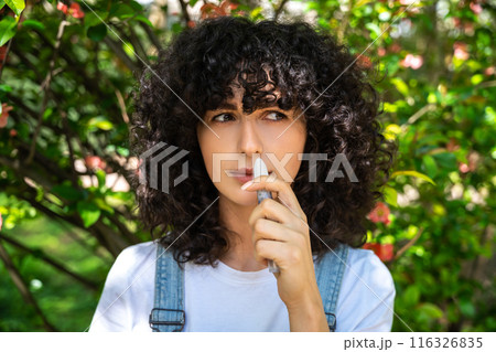 Dark-haired young woman using nasal spray while having allergy symptoms 116326835