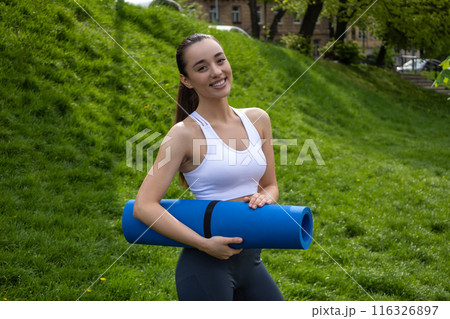 Fit athletic woman with karemat for outdoor yoga exercising 116326897
