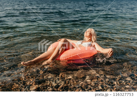 A woman is floating on a red inflatable raft in the ocean A woman is floating on a red inflatable raft in the ocean 116327753