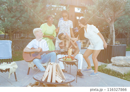 Multiracial group of friends is playing guitar, singing songs at dinner party in summer picnic 116327866