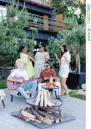 Multicultural group of people, man playing guitar and friends dancing, singing and having fun 116327868