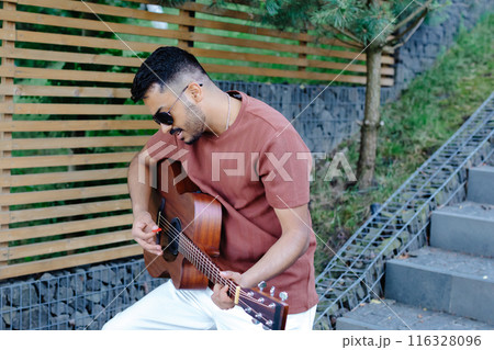 Indian hipster man playing guitar during party in the picnic in summer time Indian hipster man playing guitar during party in the picnic in summer time 116328096