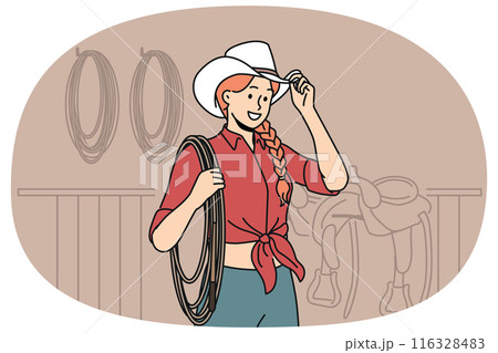 Woman jockey stands in stable wearing cowboy hat and holding long rope waiting for horses to appear. 116328483