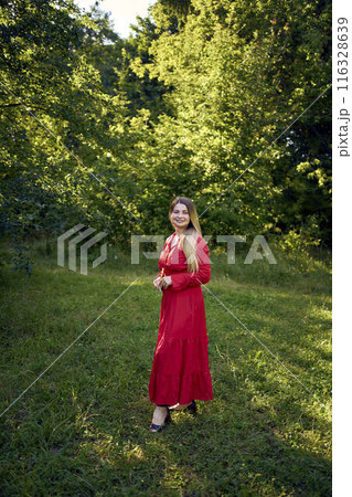 portrait of a beautiful 30-year-old woman with long blond hair in a red dress in a park 116328639