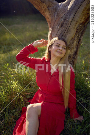 portrait of a beautiful woman with long blond hair in a red dress near a dry tree in the park portrait of a beautiful woman with long blond hair in a red dress near a dry tree in the park 116328688