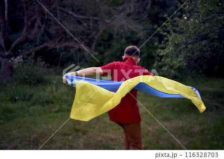 a preteen boy runs in the park with the flag of Ukraine 116328703