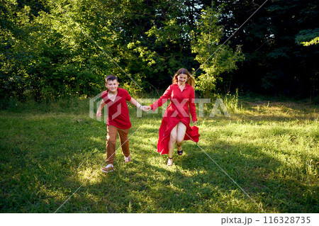 mother and preteen son in red clothes are circling and running in the garden 116328735