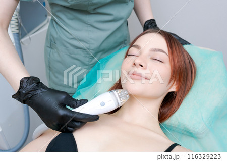 A woman is getting a facial treatment with a device that looks like a hair dryer A woman is getting a facial treatment with a device that looks like a hair dryer 116329223