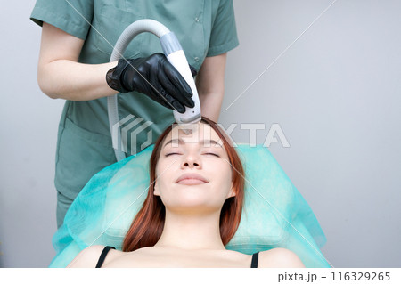 A woman is getting a facial treatment with a machine A woman is getting a facial treatment with a machine 116329265