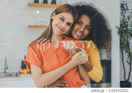 Multiethnic lesbian couple having embracing in kitchen room 116332052