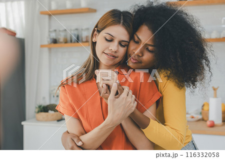 Multiethnic lesbian couple having embracing in kitchen room 116332058