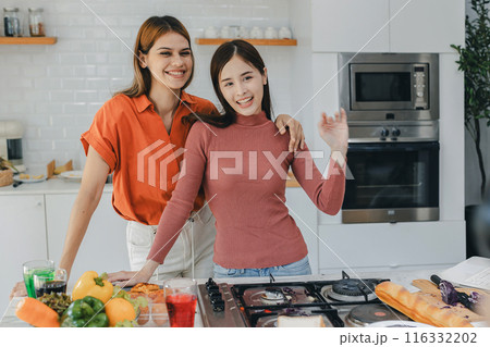 Multiethnic lesbian couple having embracing in kitchen room. 116332202