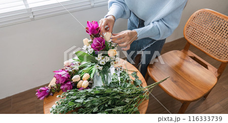 Woman Arranging Fresh Flowers in a Vase on a Wooden Table in a Bright Room 116333739