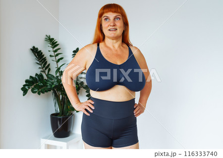 portrait red-haired middle-aged woman, plump, with large bust size, doing fitness at home 116333740