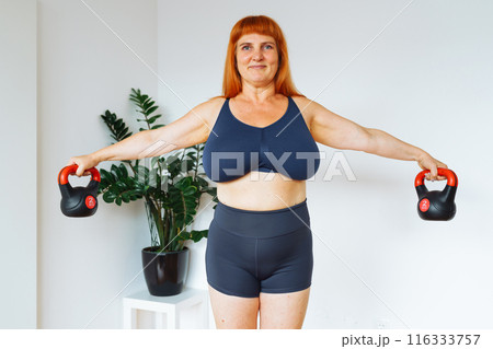 portrait red-haired middle-aged woman, plump, with large bust size, doing fitness at home portrait red-haired middle-aged woman, plump, with large bust size, doing fitness at home 116333757