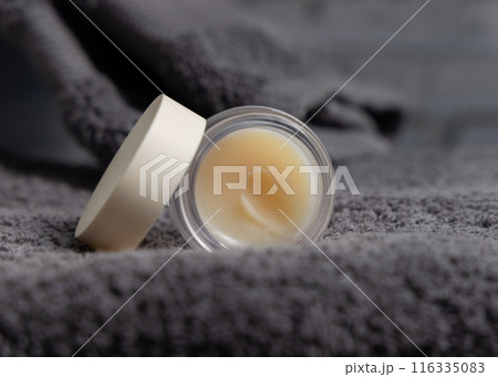 Opened lip balm jar with blank lid on dark grey bath towel closeup, cosmetic mockup Opened lip balm jar with blank lid on dark grey bath towel closeup, cosmetic mockup 116335083