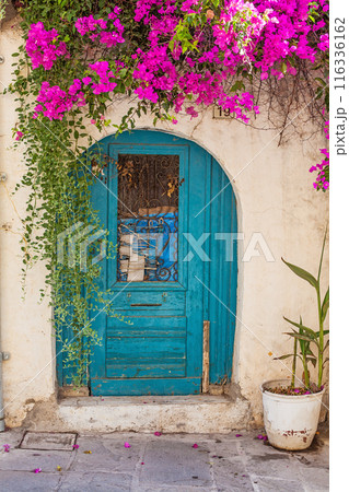 Facade of old traditional Greek building with beautiful pink flowers. Greece door Facade of old traditional Greek building with beautiful pink flowers. Greece door 116336162