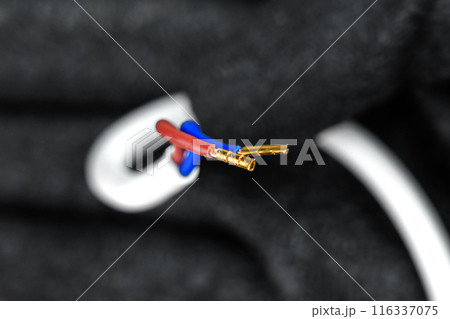 Electrical wires with exposed copper terminals of Insulated white cable in the hand of an electrician wearing black protective gloves closeup 116337075