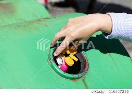 Female Hand throwing plastic bottle caps into an urban recycling bin. Recycle and reuse concept for an environmentally and globally friendly approach 116337256