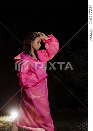 A glamour woman in a pink raincoat is spraying water from a hose A glamour woman in a pink raincoat is spraying water from a hose 116337284