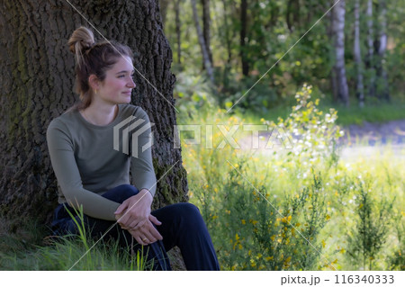 A woman relaxing by a tree in nature, enjoying the calm environment on a sunny day 116340333