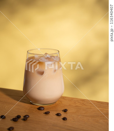 Iced coffee with milk in a glass with ice cubes and grains on a yellow background with shadows. Iced coffee with milk in a glass with ice cubes and grains on a yellow background with shadows. 116340407