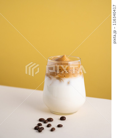 Dalgona coffee with milk in a glass with ice cubes and grains on a yellow background.  116340417