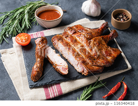 Roasted chicken legs bbq with sauce, tomato and fresh herb on a black slate on a dark background. Roasted chicken legs bbq with sauce, tomato and fresh herb on a black slate on a dark background. 116340418