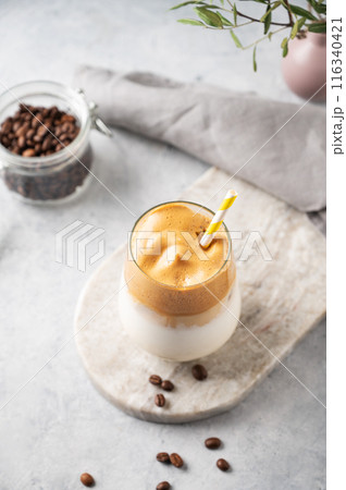 Dalgona coffee with foam in a glass with coffee beans on light marble background with branches. Dalgona coffee with foam in a glass with coffee beans on light marble background with branches. 116340421