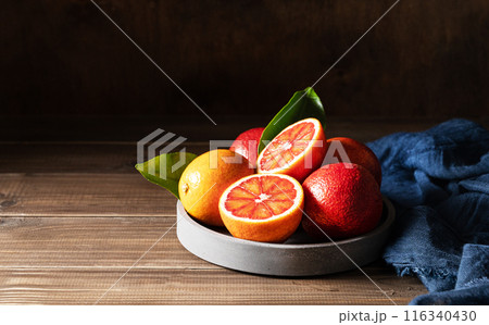 Juicy red oranges in a concrete bowl with a blue napkin on a dark wooden background. Juicy red oranges in a concrete bowl with a blue napkin on a dark wooden background. 116340430