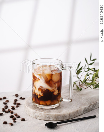 Iced coffee in a glass with cream, ice cubes and grains on a light marble background  116340436