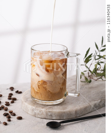 Iced coffee in a glass with pour cream, ice cubes and grains on a light marble background Iced coffee in a glass with pour cream, ice cubes and grains on a light marble background 116340438