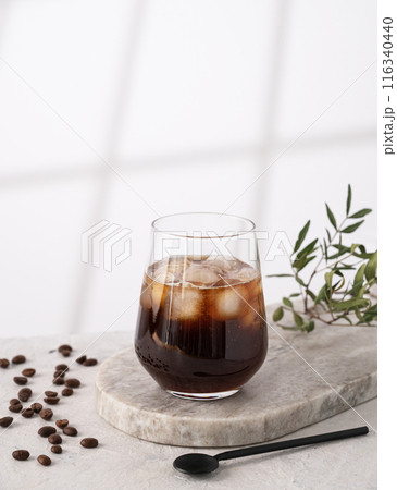 Iced coffee in a glass with ice cubes and grains on a light marble background with morning shadows.  116340440