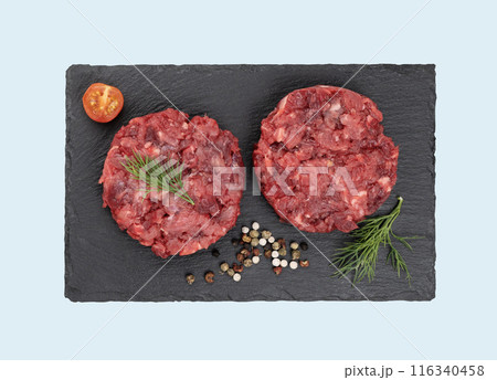 Burger patties made of raw ground beef on a black slate board with tomatoes and spices. Burger patties made of raw ground beef on a black slate board with tomatoes and spices. 116340458