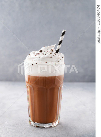Hot chocolate with whipped cream in a tall glass on a blue background. Front view and copy space Hot chocolate with whipped cream in a tall glass on a blue background. Front view and copy space 116340474