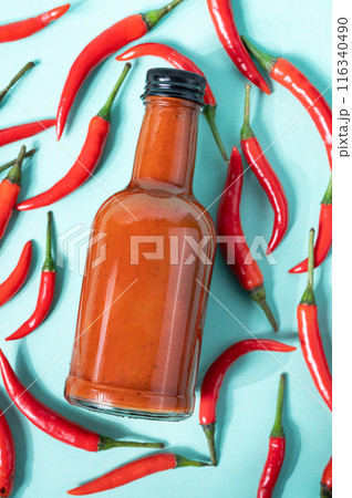 Hot chili sauce in a bottle on a bright blue background with fresh red pepper.  116340490