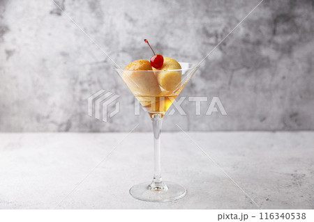 Neapolitan Rum baba (or baba au rum) in a martini glass with a cocktail cherry on a gray background. Small yeast cakes soaked in rum syrup. Traditional Italian pastry. Close-up, selective focus. Neapolitan Rum baba (or baba au rum) in a martini glass with a cocktail cherry on a gray background. Small yeast cakes soaked in rum syrup. Traditional Italian pastry. Close-up, selective focus. 116340538
