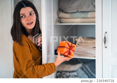 Funny girl makes surprise, hides a gift in the closet. Funny girl makes surprise, hides a gift in the closet. 116340718