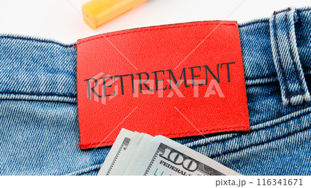 Conceptual RETIREMENT symbol. Copy space. RETIREMENT on the red leather label of jeans on a white background in a composition with American dollars Conceptual RETIREMENT symbol. Copy space. RETIREMENT on the red leather label of jeans on a white background in a composition with American dollars 116341671