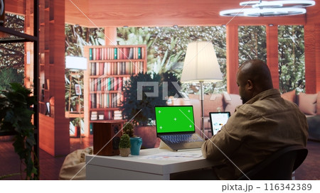 Businessman reviewing statistics reports next to an isolated mockup screen at home office, adviser calculating budget in order to expand the enterprise activity. Finance and economy. Camera B. Businessman reviewing statistics reports next to an isolated mockup screen at home office, adviser calculating budget in order to expand the enterprise activity. Finance and economy. Camera B. 116342389