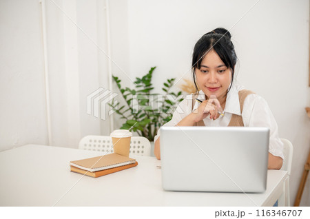 A beautiful Asian woman working remotely from a minimal white coffee shop, working on her laptop. A beautiful Asian woman working remotely from a minimal white coffee shop, working on her laptop. 116346707